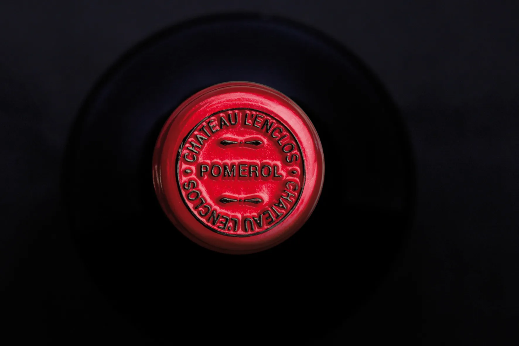 Top-down view of a wine bottle foil capsule in red, embossed with “Chateau L’Enclos” and “Pomerol.”