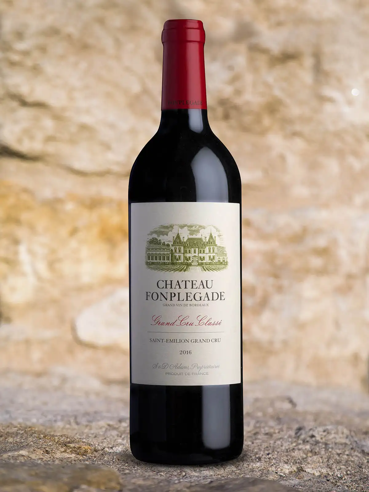 A bottle of Château Fonplégade 2016 Saint-Émilion Grand Cru red wine stands on a stone surface with a textured beige background.