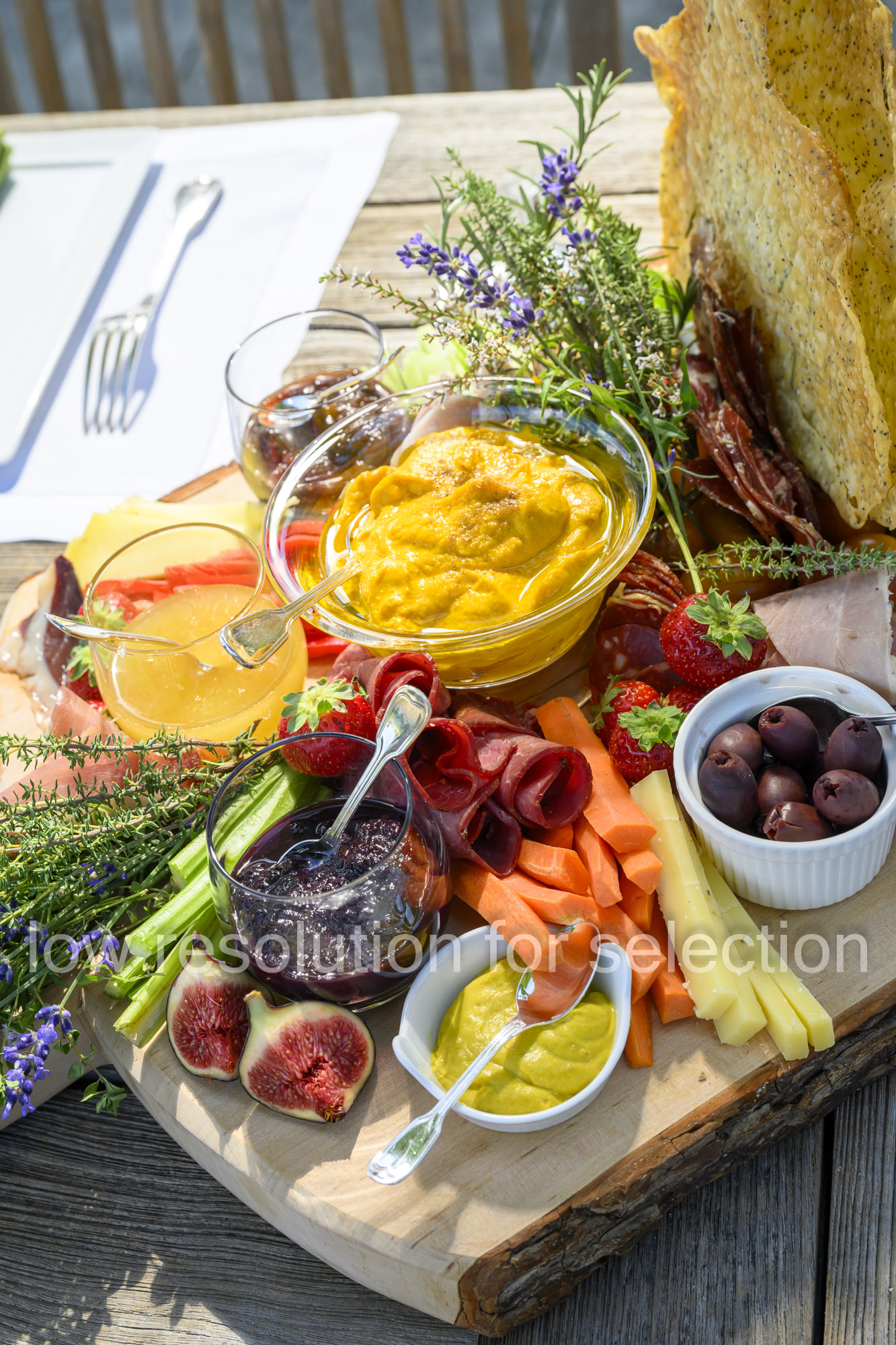 A charcuterie board featuring bowls of dips, spreads, cured meats, sliced vegetables, cheese, olives, fresh figs, strawberries, and large crackers.