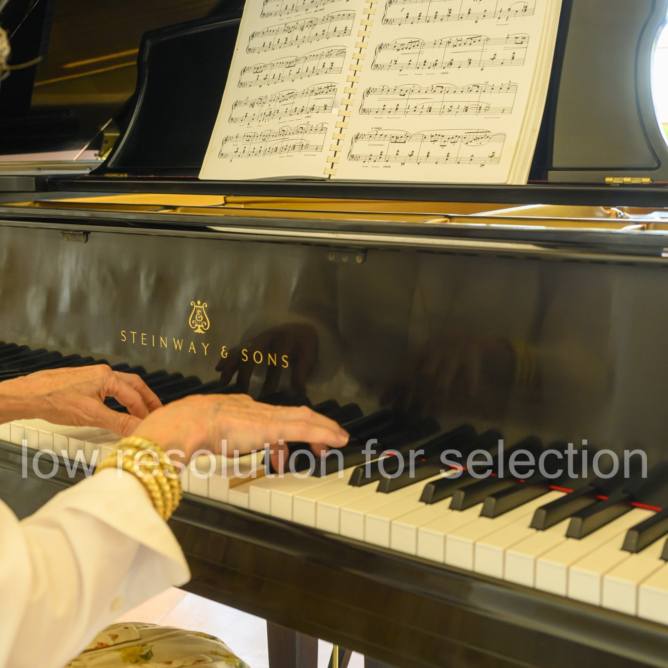 Hands of a person playing a Steinway & Sons grand piano with sheet music on the stand.