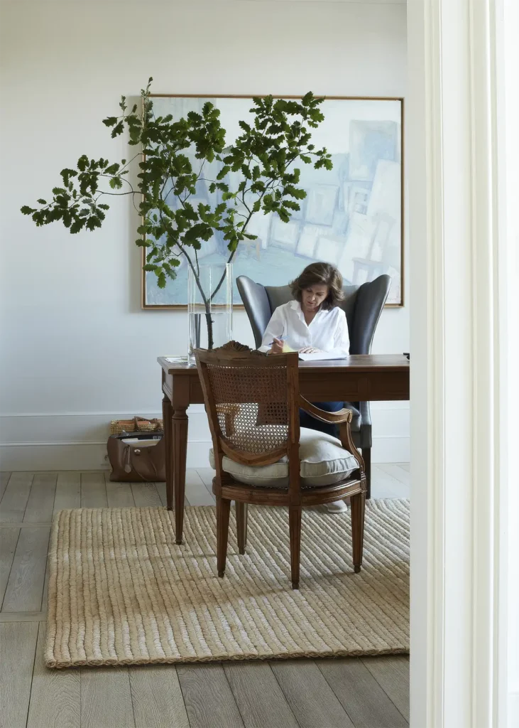 A woman sits at a wooden desk writing in a notebook.